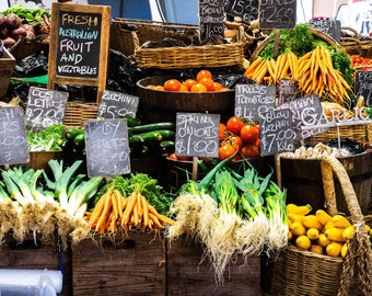 May include: A vibrant display of fresh produce at a market. Wooden crates and woven baskets overflow with colorful fruits and vegetables, including carrots, tomatoes, zucchini, and leeks. Signs indicate the items are Australian.