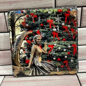May include: A bronze statue of a woman sitting on a crescent moon, reaching up to touch a Christmas tree decorated with red bows, red ornaments, and silver ornaments.