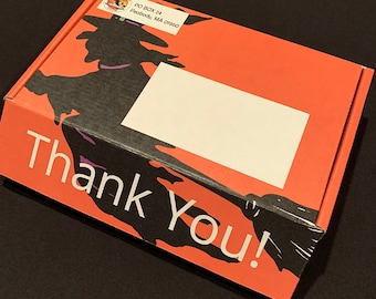 Könnte beinhalten: Eine rote und schwarze Schachtel mit einer Hexensilhouette und dem Text "Danke!" auf der Vorderseite. Die Schachtel hat ein weißes Etikett mit dem Text "PO BOX 24 Peabody, MA 01960".