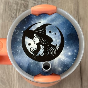 May include: A pink and white tumbler lid with a black and white illustration of a witch with a crescent moon and stars on a blue galaxy background.
