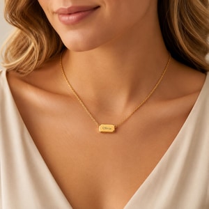 Può includere: Una collana color oro con un piccolo ciondolo rettangolare orizzontale dagli angoli arrotondati. Il ciondolo presenta l'incisione del nome Olivia in un carattere scuro e nitido. Il ciondolo è sospeso a una sottile catenina color oro.