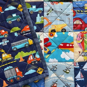 May include: A blue and white patchwork quilt with various designs, including construction vehicles, airplanes, hot air balloons, and sailboats. The quilt is made of different fabrics and has a denim border.