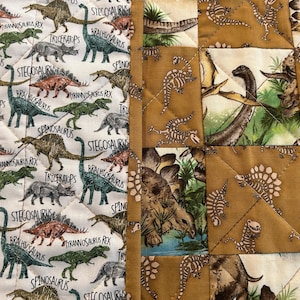 Könnte beinhalten: Gesteppter Stoff mit Dinosaurier-Motiv. Die linke Seite hat einen weißen Hintergrund mit verschiedenen Dinosauriern in Grün, Braun und Grau, mit Textbeschriftungen. Die rechte Seite hat einen braunen Hintergrund mit Dinosaurier-Illustrationen.