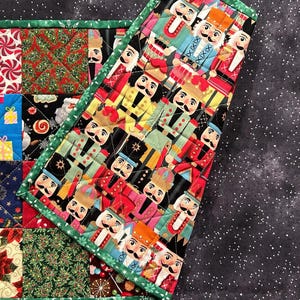 May include: A quilted Christmas placemat with a green border. One section features a pattern of nutcrackers, while the other has squares with holiday-themed designs like candy canes, gifts, and poinsettias.