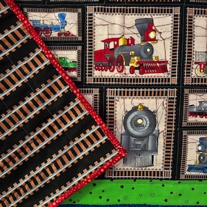 May include: A quilted fabric featuring a repeating pattern of vintage train illustrations in various colors, set within rectangular frames. The quilt has a black border with brown and black railroad tracks, a red border, and green and blue sections.