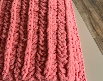Könnte beinhalten: Eine weiche, rosafarbene Strickdecke mit einem Zopfmuster.