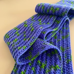 May include: A blue and green crocheted scarf with a textured pattern. The scarf is folded in half and the ends are visible.