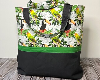 May include: A black and green tote bag with a white background featuring a tropical print of toucans and parrots. The bag has a green stripe and black bottom.