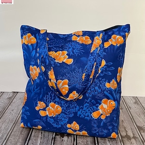 May include: A blue tote bag with a pattern of orange and white clownfish swimming in coral reefs. The bag has two black straps.