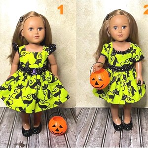 May include: Two dolls wearing Halloween-themed dresses. The dresses are lime green with a black cat print and black polka dot accents. One doll holds an orange jack-o'-lantern bucket. The dolls are wearing black shoes.