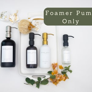 Puede incluir: Cuatro botellas de vidrio negro, blanco y transparente con etiquetas que dicen "Jab&oacute;n para platos" y "Loci&oacute;n para manos". Las botellas tienen bombas de espuma negras, doradas y plateadas. El texto "Foamer Pump Only" est&aacute; escrito en verde sobre un fondo blanco.