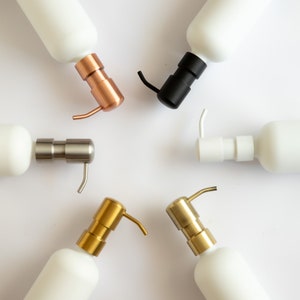 Puede incluir: Cinco dispensadores de jab&oacute;n de cer&aacute;mica blanca con bombas de diferentes colores. Las bombas son doradas, plateadas, negras, cobre y oro rosa.