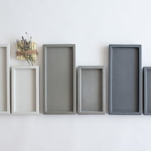Peut inclure: Six plateaux rectangulaires en b&eacute;ton de diff&eacute;rentes tailles. Les plateaux sont en deux nuances de gris et de blanc. Les plateaux sont dispos&eacute;s en rang&eacute;e du plus grand au plus petit.