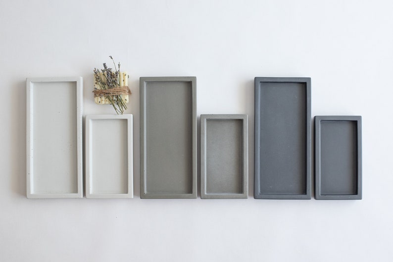 Peut inclure: Six plateaux rectangulaires en b&eacute;ton de diff&eacute;rentes tailles. Les plateaux sont en deux nuances de gris et de blanc. Les plateaux sont dispos&eacute;s en rang&eacute;e du plus grand au plus petit.