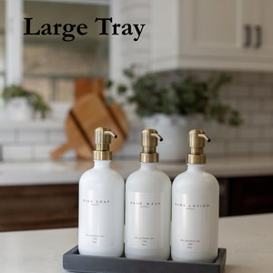 Peut inclure: Trois flacons pompe en c&eacute;ramique blanche avec des bouchons dor&eacute;s sur un plateau rectangulaire gris. Les flacons sont &eacute;tiquet&eacute;s "Savon &agrave; vaisselle", "Lavage des mains" et "Lotion pour les mains".