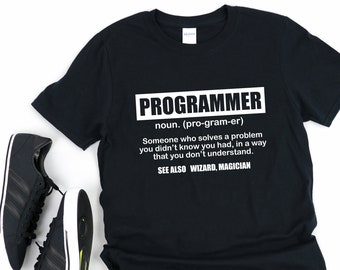 May include: Black t-shirt with white text that reads "PROGRAMMER noun. (pro-gram-er) Someone who solves a problem you didn't know you had, in a way that you don't understand. SEE ALSO WIZARD, MAGICIAN"