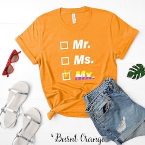 May include: Burnt orange t-shirt with a white box around the words "Mr." "Ms." and "Mx." The box around "Mx." is checked and has a purple and yellow stripe.