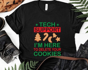 Può includere: Maglietta nera con un design a tema natalizio che dice "Tech Support I'm Here To Delete Your Cookies". Il design presenta biscotti di pan di zenzero, una canna di zucchero e una campana.
