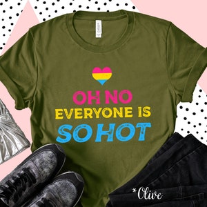 May include: Olive green t-shirt with the text "OH NO EVERYONE IS SO HOT" in pink, yellow, and blue. A pansexual pride heart graphic is above the text. The shirt is displayed with black jeans and sneakers.