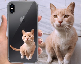 May include: A clear phone case with a black phone inside. A cartoon image of a ginger cat is on the back of the phone case. A ginger cat is sitting on a surface in the background.
