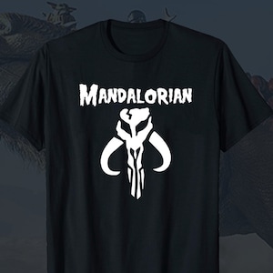 Puede incluir: Camiseta negra con un s&iacute;mbolo mandaloriano blanco y el texto "MANDALORIAN" impreso en la parte delantera.