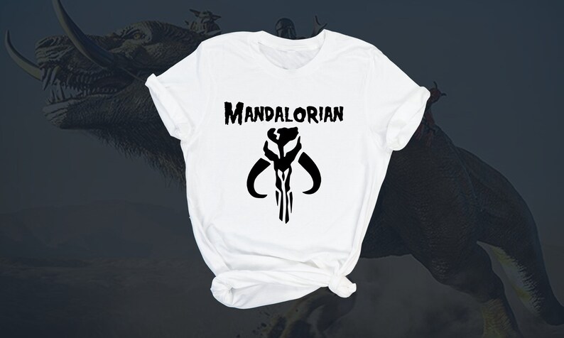 Puede incluir: Camiseta blanca con un s&iacute;mbolo mandaloriano negro y el texto "MANDALORIAN" impreso en la parte delantera.