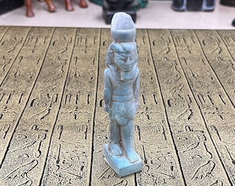 May include: A small blue figurine of an Egyptian god with a headdress. The figurine is standing on a table with a pattern of hieroglyphs.