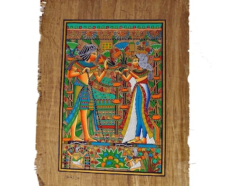 May include: A hand-painted papyrus scroll depicting an Egyptian scene with two figures in colorful clothing standing in a garden with flowers and plants. The scroll is framed with a brown border and has the text "عادى نور" at the bottom.