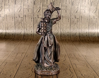 May include: Bronze figurine of an Egyptian goddess holding a staff and a crown. The figurine is standing on a base with the word "Bastet" inscribed on it.