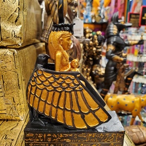May include: Gold and black statue of the Egyptian goddess Isis with a winged figure and hieroglyphics on the base.