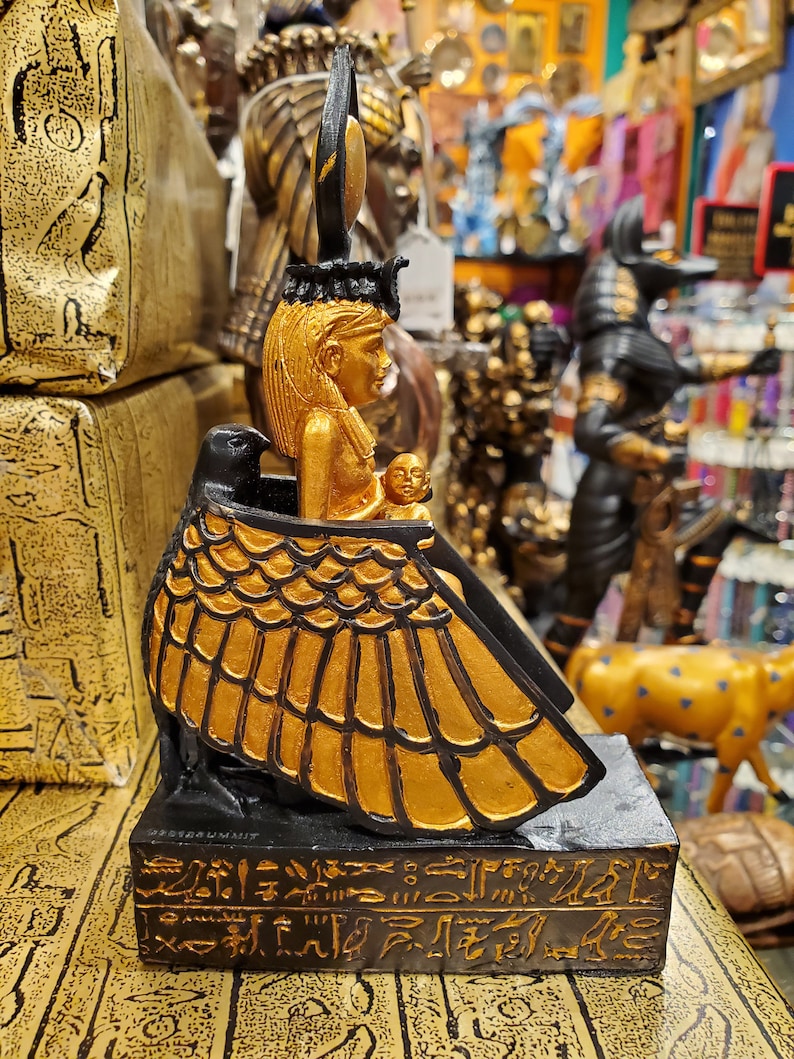 May include: Gold and black statue of the Egyptian goddess Isis with a winged figure and hieroglyphics on the base.