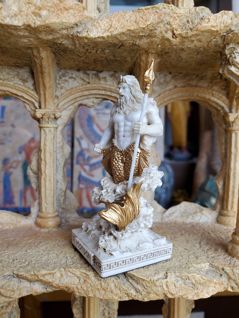 May include: White figurine of Poseidon, the Greek god of the sea, holding a trident. He is standing on a wave with a fish tail. The figurine is on a white base with a Greek key design.