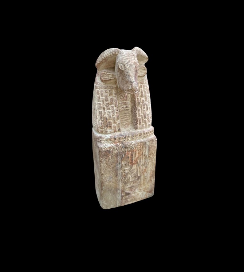 May include: A small, carved stone statue of an Egyptian god with a bull's head. The statue is in a standing position and has a rectangular base.