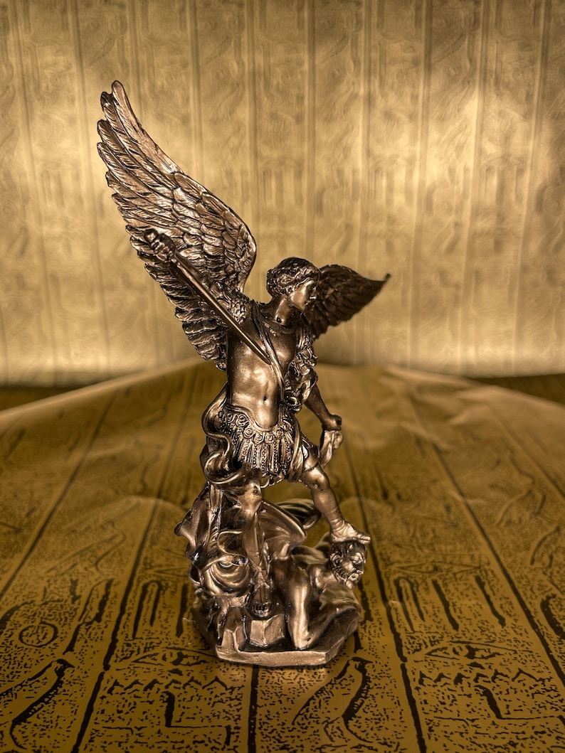 May include: A bronze statue of an angel with wings spread, holding a sword and standing on a defeated demon. The statue is on a patterned surface.