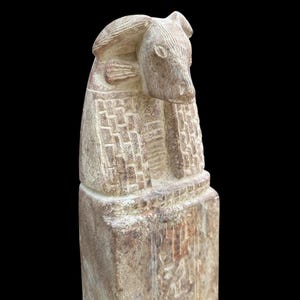 May include: A carved stone statue of an Egyptian god with a bull's head. The statue is weathered and has a light brown colour.