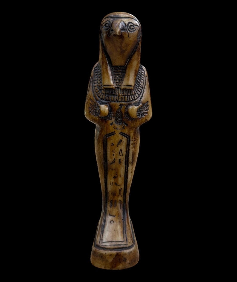 May include: A carved wooden figurine of an Egyptian god with a falcon head, wearing a traditional headdress and holding a staff. The figurine is decorated with hieroglyphs.