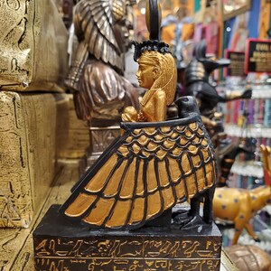 May include: Gold and black figurine of the Egyptian goddess Isis, seated on a throne with a winged figure, with hieroglyphics on the base.