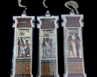 Könnte beinhalten: Drei ägyptisch inspirierte Lesezeichen mit Quaste. Jedes Lesezeichen zeigt eine andere Szene mit Hieroglyphen und Figuren in bunten Kleidern.