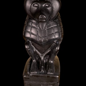 May include: Black stone sculpture of a monkey wearing a patterned garment, sitting on a base with the inscription "TOYET".