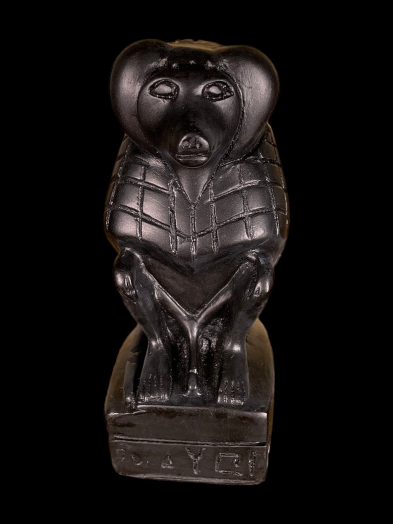 May include: Black stone sculpture of a monkey wearing a patterned garment, sitting on a base with the inscription "TOYET".
