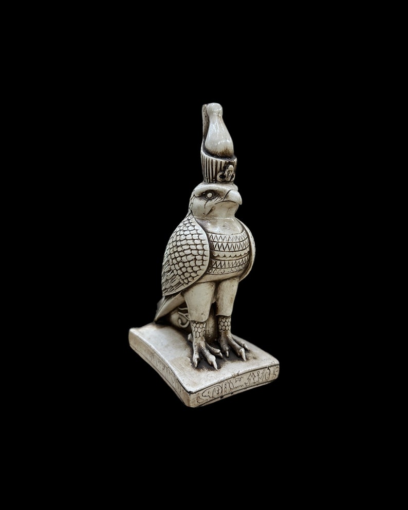 K&ouml;nnte beinhalten: Eine detaillierte, cremefarbene Statue eines Falken, m&ouml;glicherweise Horus, der &auml;gyptische Gott. Der Falke steht auf einem rechteckigen Sockel mit Hieroglyphen. Die Statue weist aufwendige Details auf, darunter Federn und Kopfschmuck.
