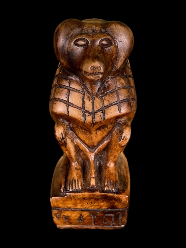 May include: A small, wooden sculpture of a monkey sitting on a base. The monkey is carved in a realistic style and has a brown color. The base is inscribed with the text "SAY."