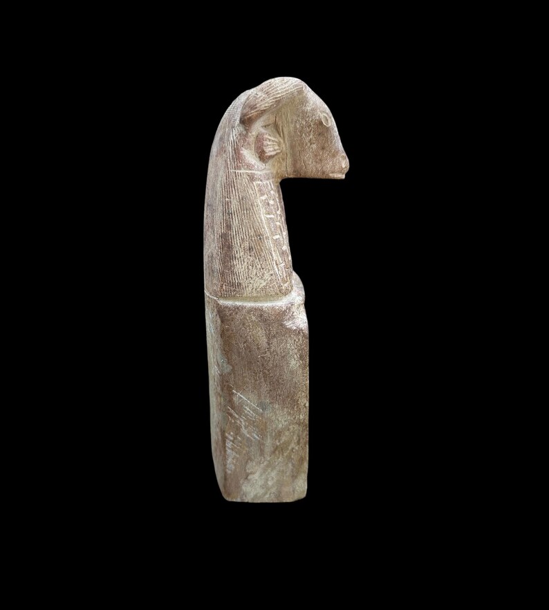 May include: A carved stone sculpture of a ram's head with a long neck. The sculpture is made of a light brown stone with a rough texture.
