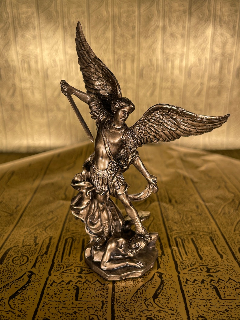 May include: A bronze statue of an angel with wings spread, standing on a defeated figure. The angel is holding a sword in its right hand and has a determined expression on its face.