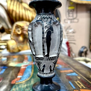 Op de afbeelding: Zwarte en witte decoratieve vaas met een Egyptisch hiërogliefenontwerp. De vaas is gemaakt van glad, gepolijst steen en heeft een ronde basis.