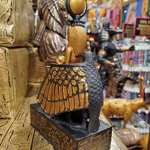 May include: A gold and black figurine of the Egyptian goddess Bastet, depicted as a cat with a human head and a sun disk on her head. The figurine is standing on a base with hieroglyphics.