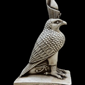 K&ouml;nnte beinhalten: Eine detaillierte, cremefarbene Statue einer falkenk&ouml;pfigen Gottheit, m&ouml;glicherweise Horus, mit aufwendigen Feder- und Schuppendetails. Die Statue steht auf einem rechteckigen Sockel mit Hieroglyphen und dem Horusauge.