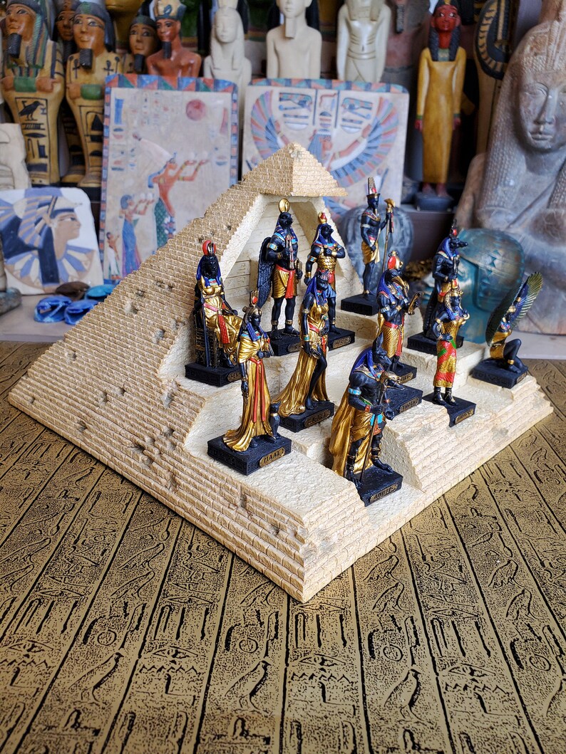 May include: A pyramid-shaped display stand with a collection of small, colorful figurines of Egyptian gods and goddesses. The figurines are arranged in a circle around the base of the pyramid, with the god Anubis at the top.