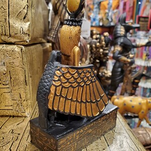 May include: A small black and gold statue of the Egyptian goddess Bastet, depicted as a woman with a cat's head and wings. The statue is standing on a base with hieroglyphics.