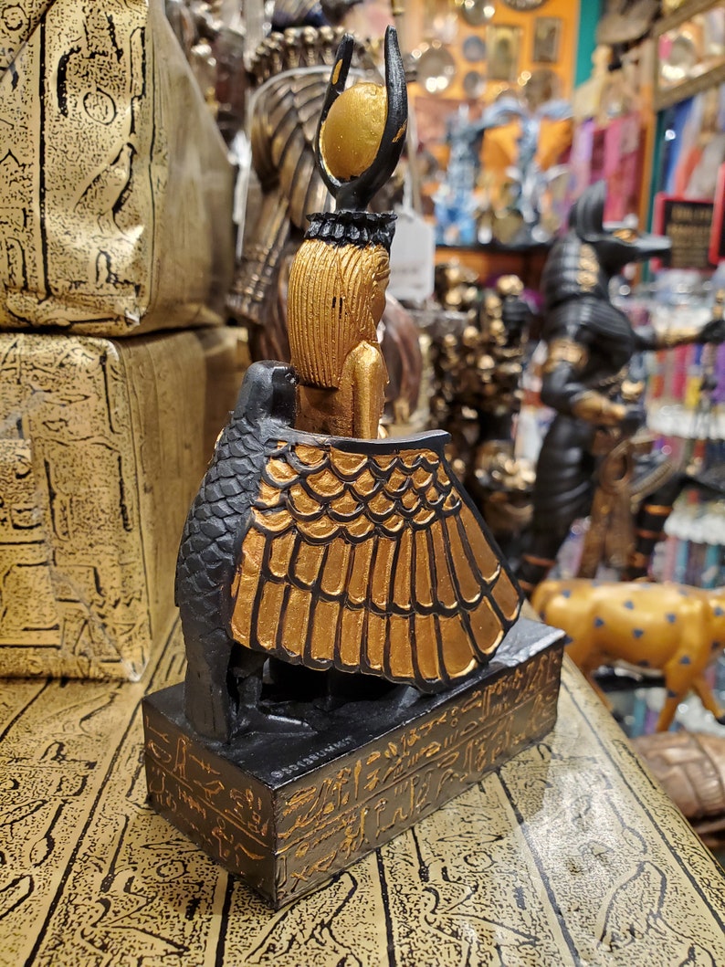 May include: A small black and gold statue of the Egyptian goddess Bastet, depicted as a woman with a cat's head and wings. The statue is standing on a base with hieroglyphics.